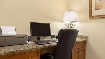 A hotel room desk with a desktop computer, a printer, a lamp, and a chair.