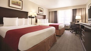 A hotel room with two beds, a desk, a chair, a television, and a window with curtains.