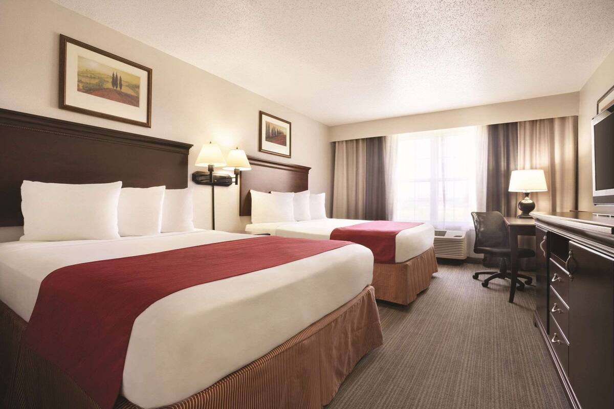 A hotel room with two beds, a desk, a chair, a television, and a window with curtains.