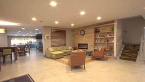 Um hall amplo com sofá, poltronas, lareira, estante de livros e escada.