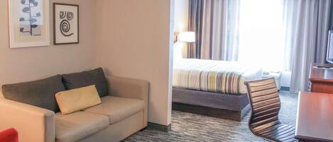 A hotel room with a sofa, a chair, a bed with striped bedding, a desk, and a TV.
