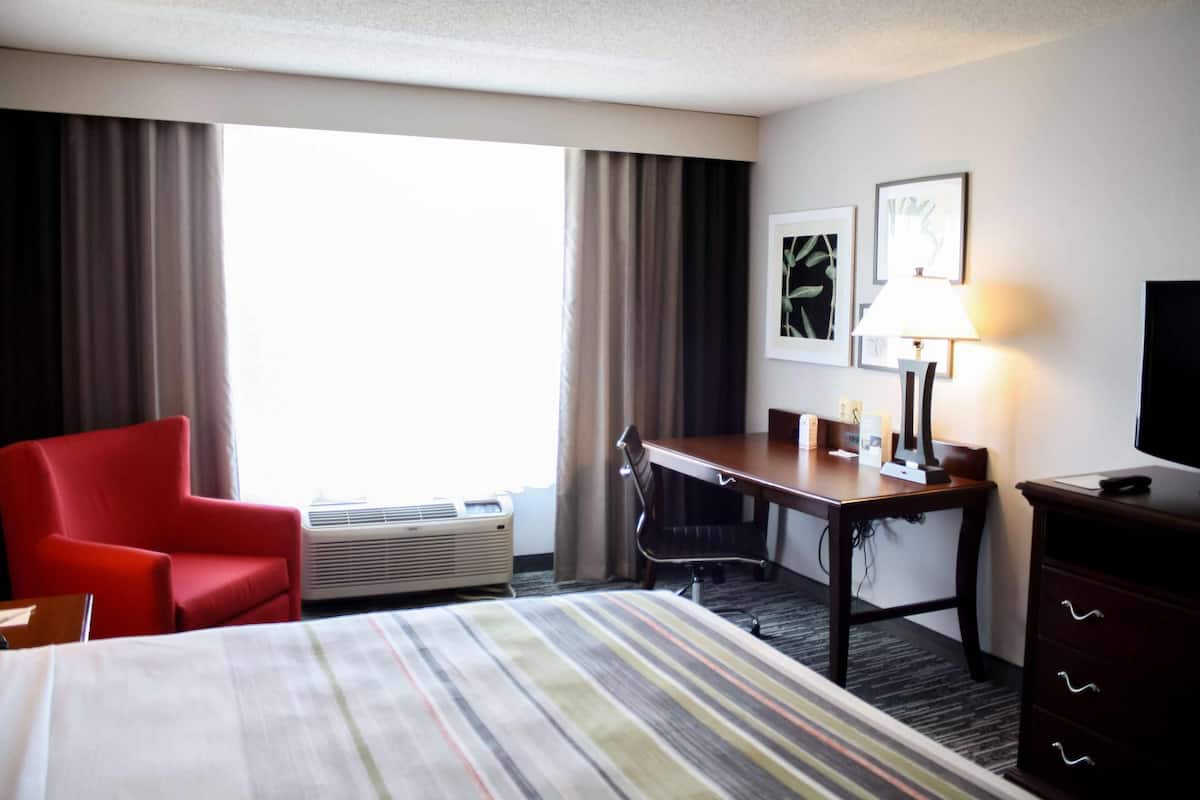 A hotel room with a bed, a desk, a chair, a TV, and a lamp.