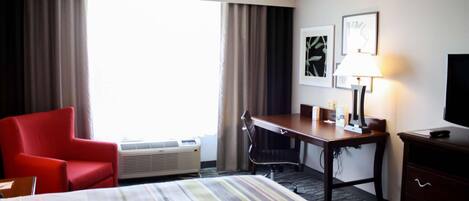 A hotel room with a bed, a desk, a chair, a TV, and a lamp.