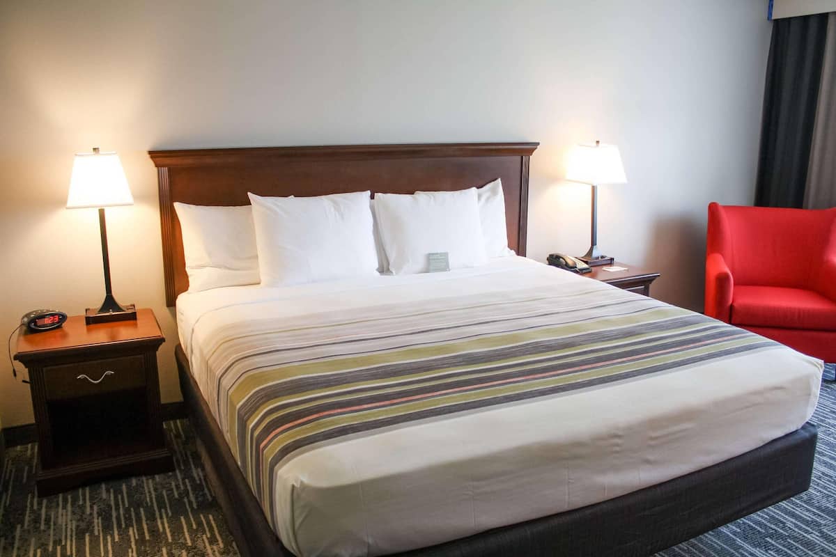A hotel room with a large bed, two bedside tables with lamps, a red chair, and a carpeted floor.