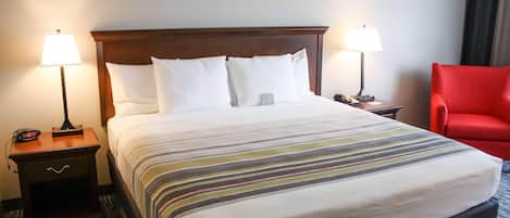 A hotel room with a large bed, two bedside tables with lamps, a red chair, and a carpeted floor.