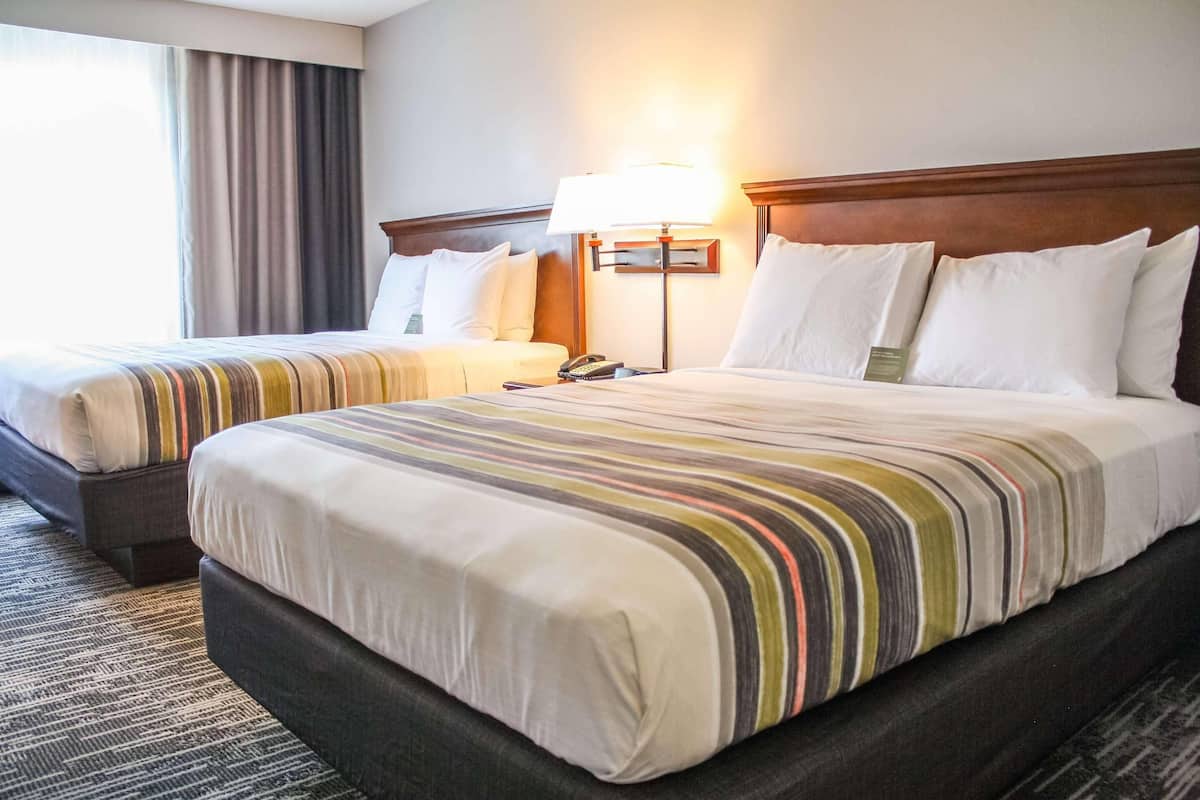 A hotel room with two beds, a bedside lamp, and a telephone on the nightstand.