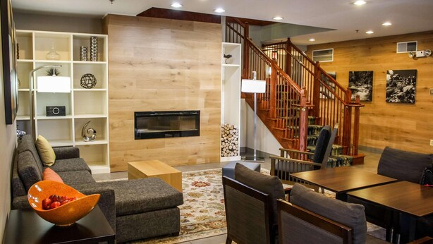 A modern living room with a sofa, ottoman, coffee table, and a TV. There is a staircase with wooden railings leading to an upper level. - Country Inn & Suites by Radisson, Washington Dulles International Airport, VA (Sterling)
