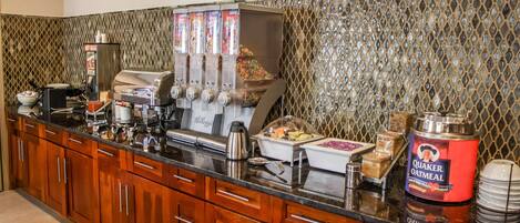 A breakfast bar with a coffee machine, juice dispensers, and a Quaker Oatmeal container.