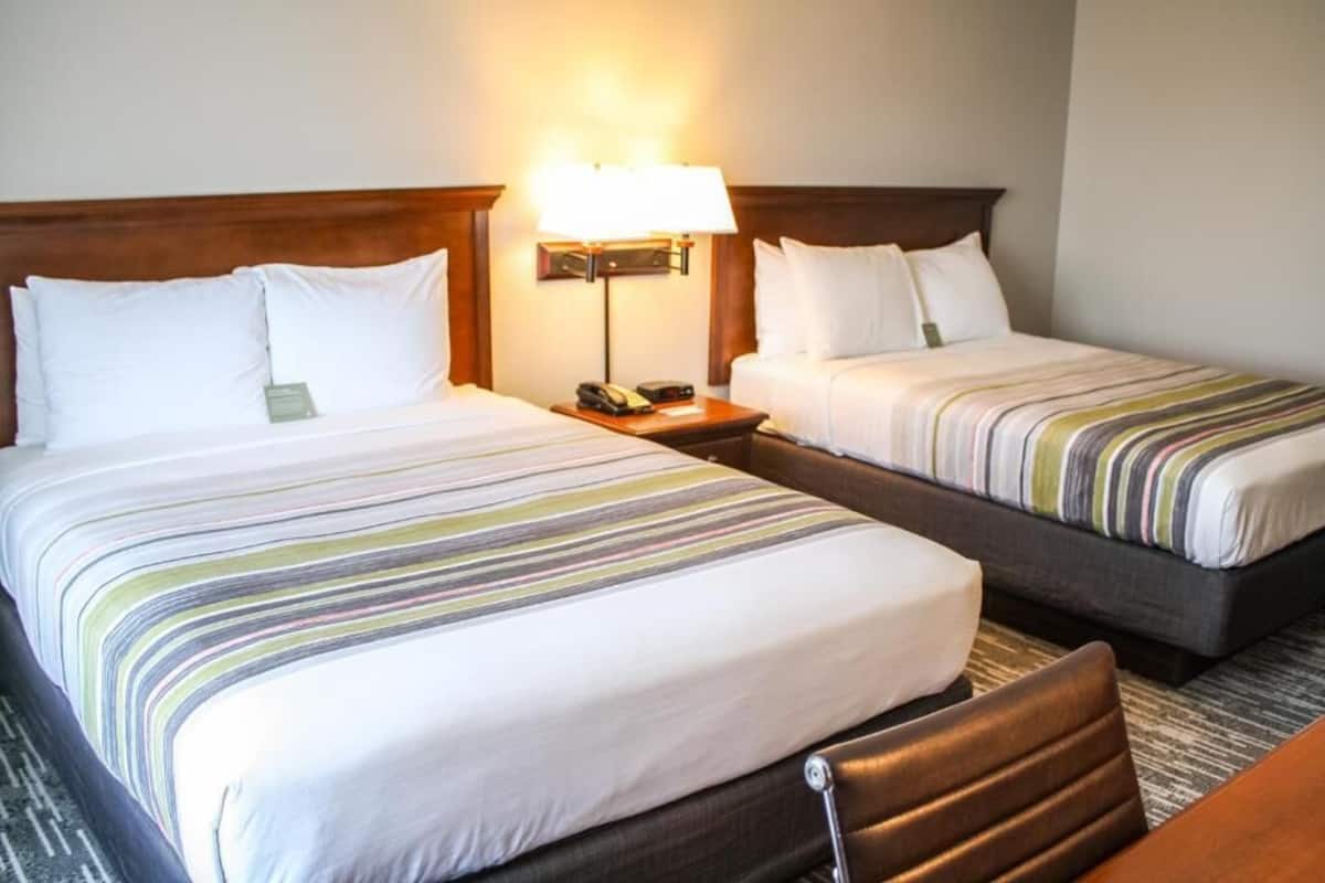 Two adjacent hotel beds with striped bedding, a bedside table with a lamp, and a wooden headboard.