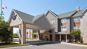 A Country Inn & Suites building with a covered entrance, stone pillars, and a flag. - Country Inn & Suites by Radisson, Washington Dulles International Airport, VA (Sterling)