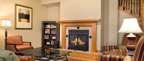 A cozy living room with a fireplace, a bookshelf, and striped armchairs.