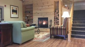 A cozy living room with a fireplace, a striped armchair, a green sofa, and a bookshelf. - Country Inn & Suites by Radisson, Salina, KS (Salina)
