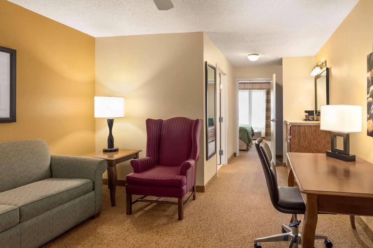 A hotel room with a sofa, a chair, a desk, and a lamp.
