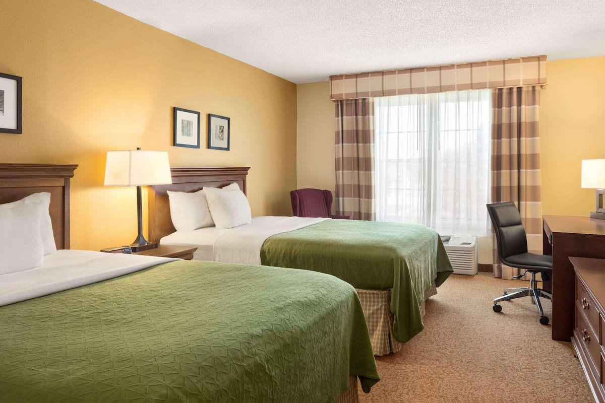 A hotel room with two beds, a desk, a chair, and a window with curtains.