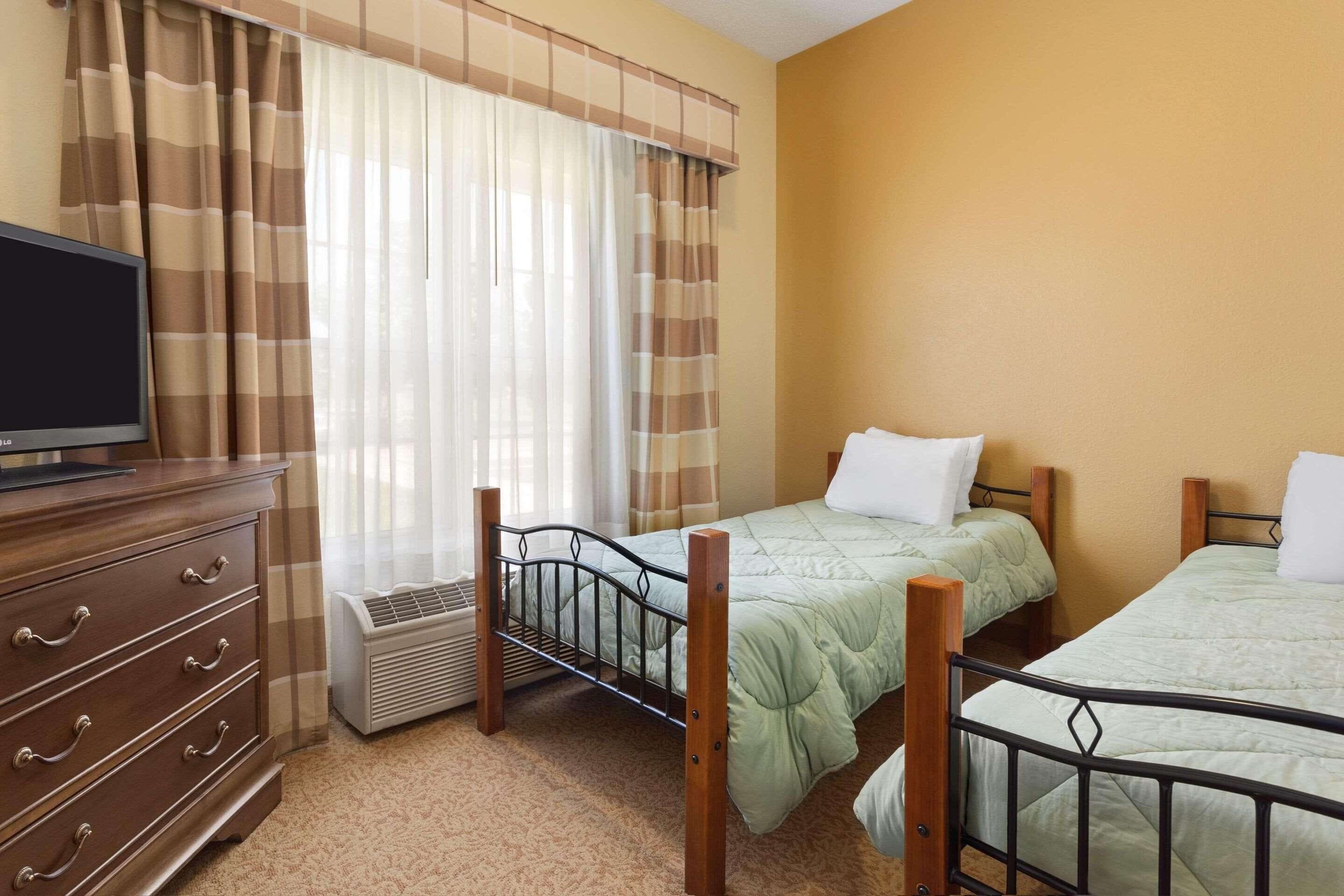 A room with two beds, a wooden dresser, a television, and a window with curtains.