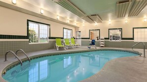 An indoor swimming pool with clear blue water, green lounge chairs, and a tiled wall with windows. - Country Inn & Suites by Radisson, Salina, KS (Salina)