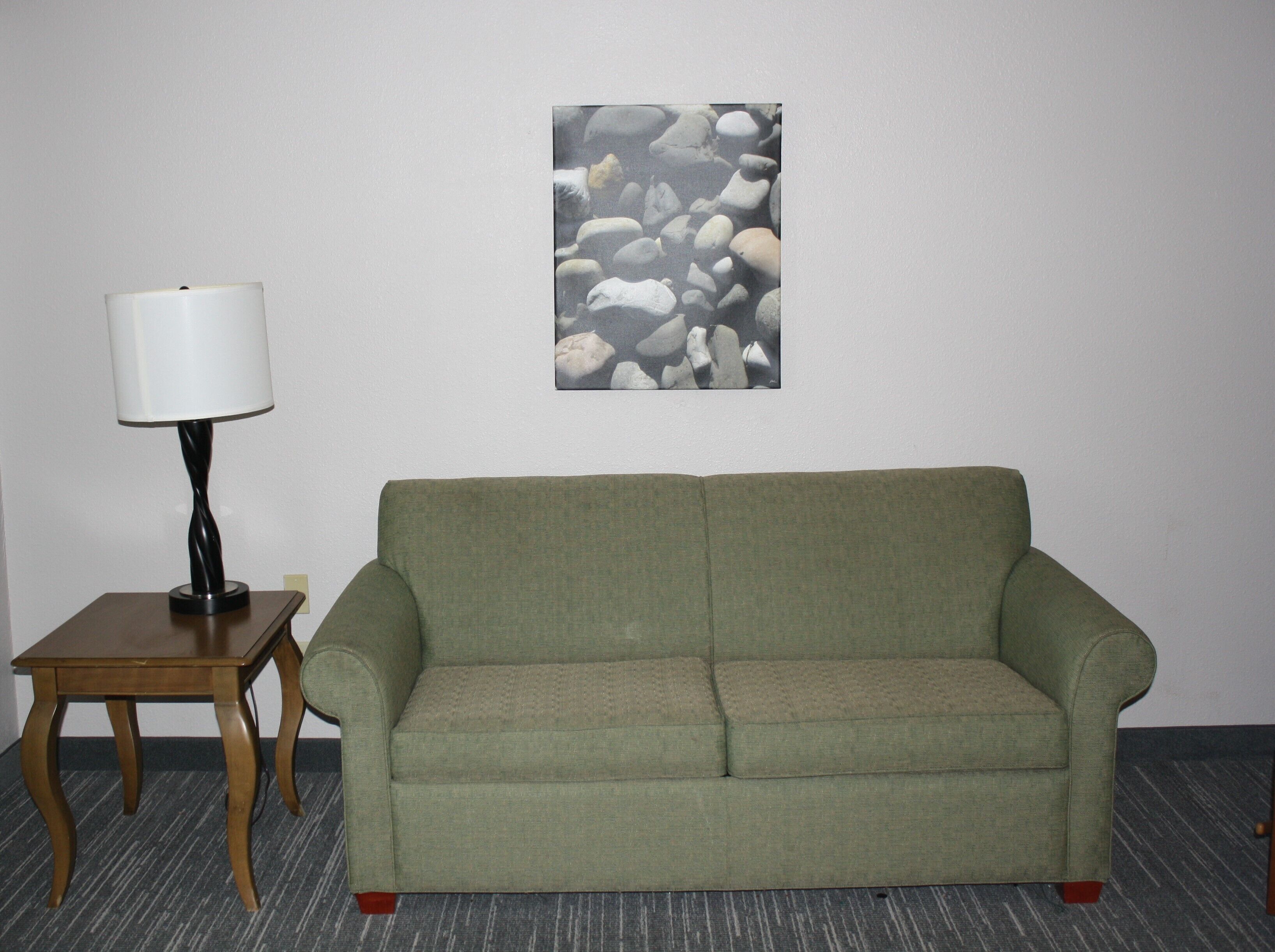 Una habitación con un sofá verde, una pequeña mesa de madera con una lámpara y una pared decorada con un arte de piedras.