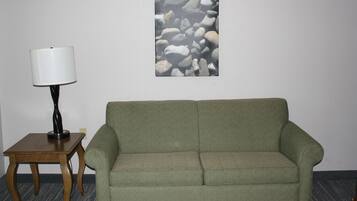 Una habitación con un sofá verde, una pequeña mesa de madera con una lámpara y una pared decorada con un arte de piedras.