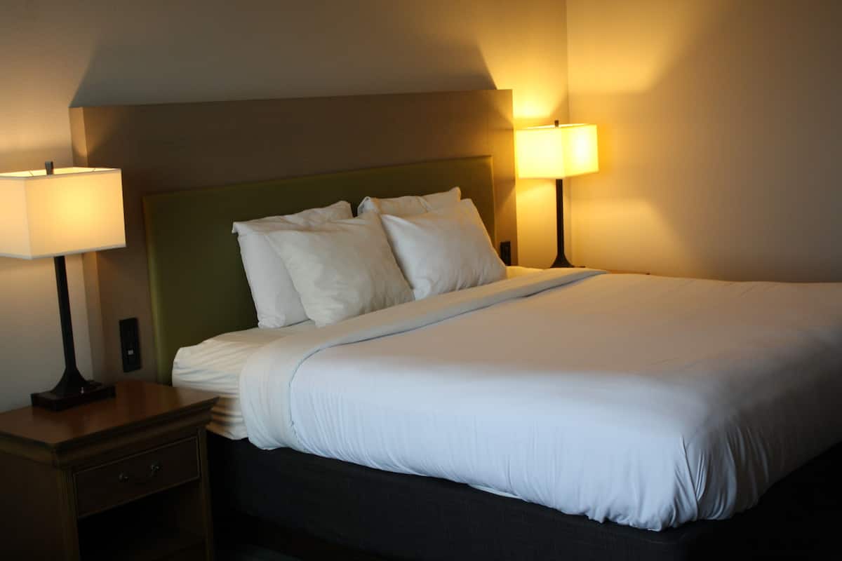 A neatly made bed with white linens and a green headboard in a hotel room.