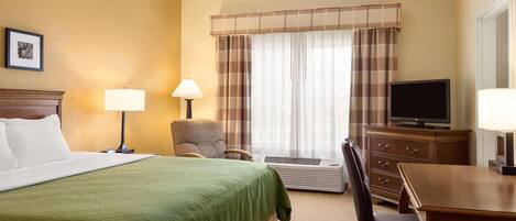 Una habitación de hotel con cama, escritorio, silla, televisión y ventana con cortinas.