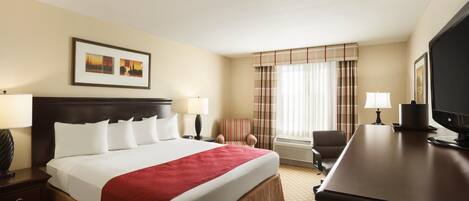 A hotel room with a large bed, a desk, a chair, a television, and a window with curtains.