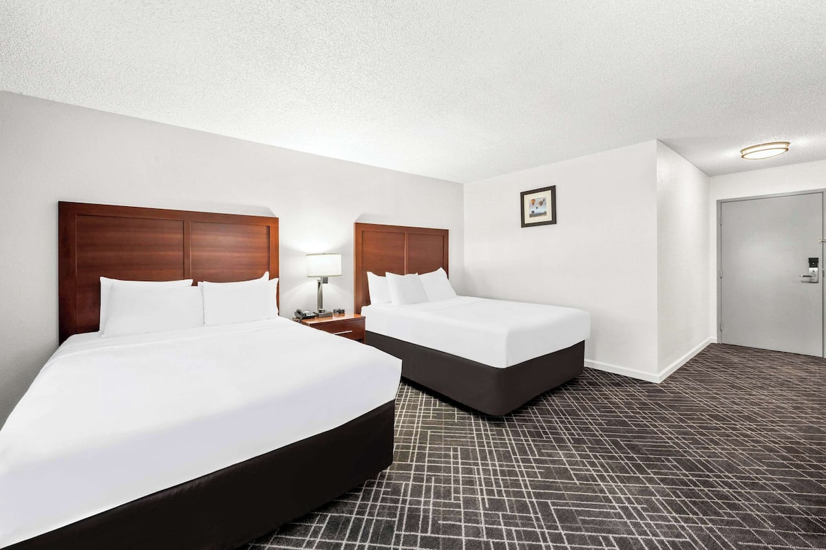 A hotel room with two beds, a nightstand with a lamp, a framed picture on the wall, and a door.