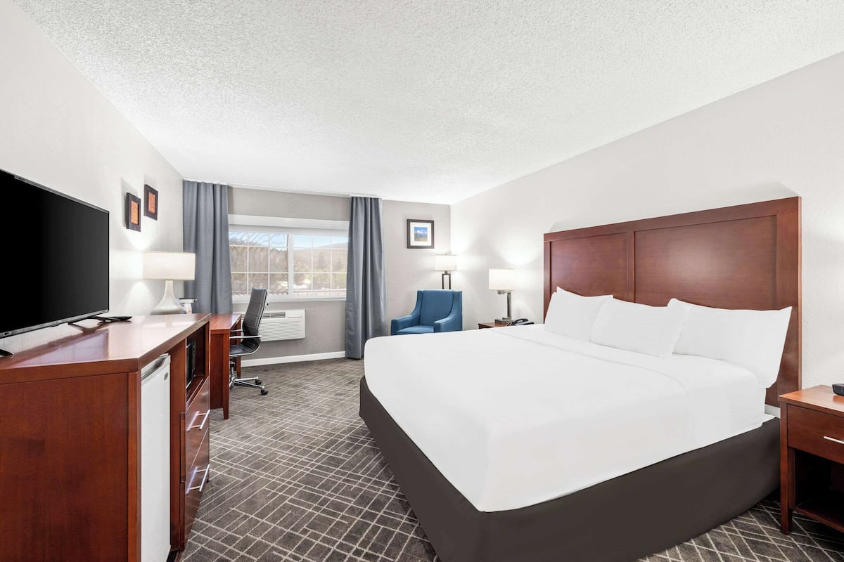 A hotel room with a large bed, a desk with a television, a chair, and a window with curtains.