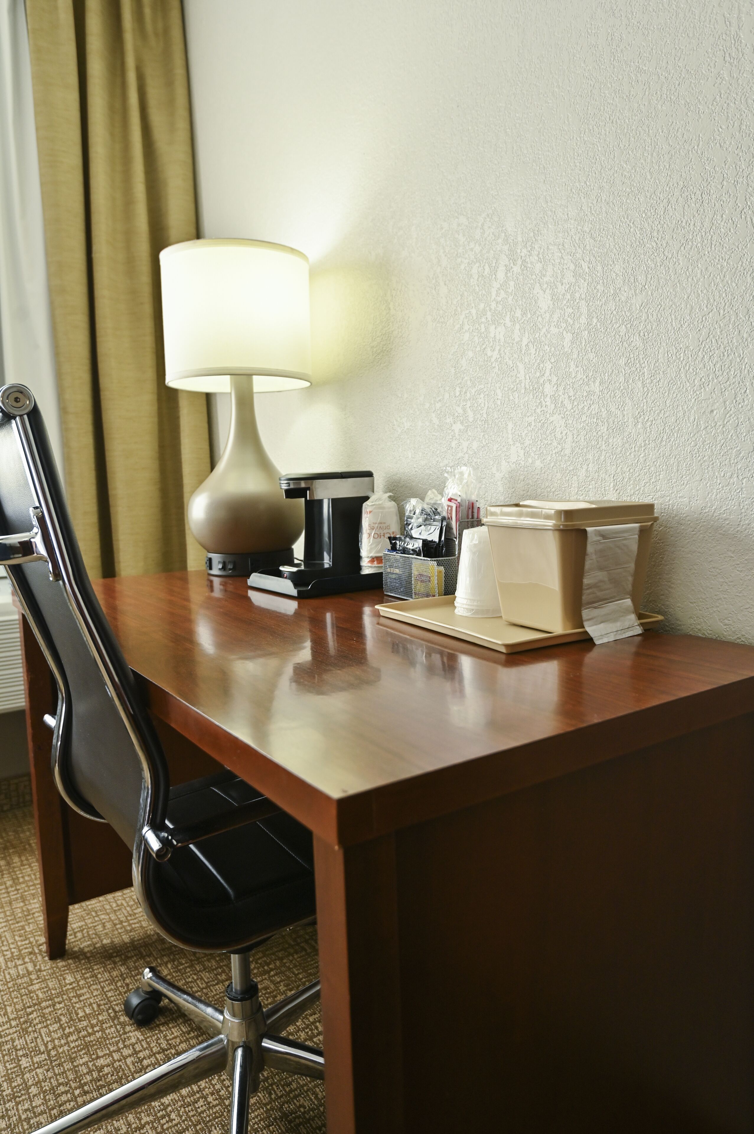 A hotel desk with a lamp, coffee maker, and toiletries.