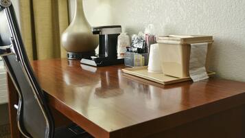A hotel desk with a lamp, coffee maker, and toiletries.