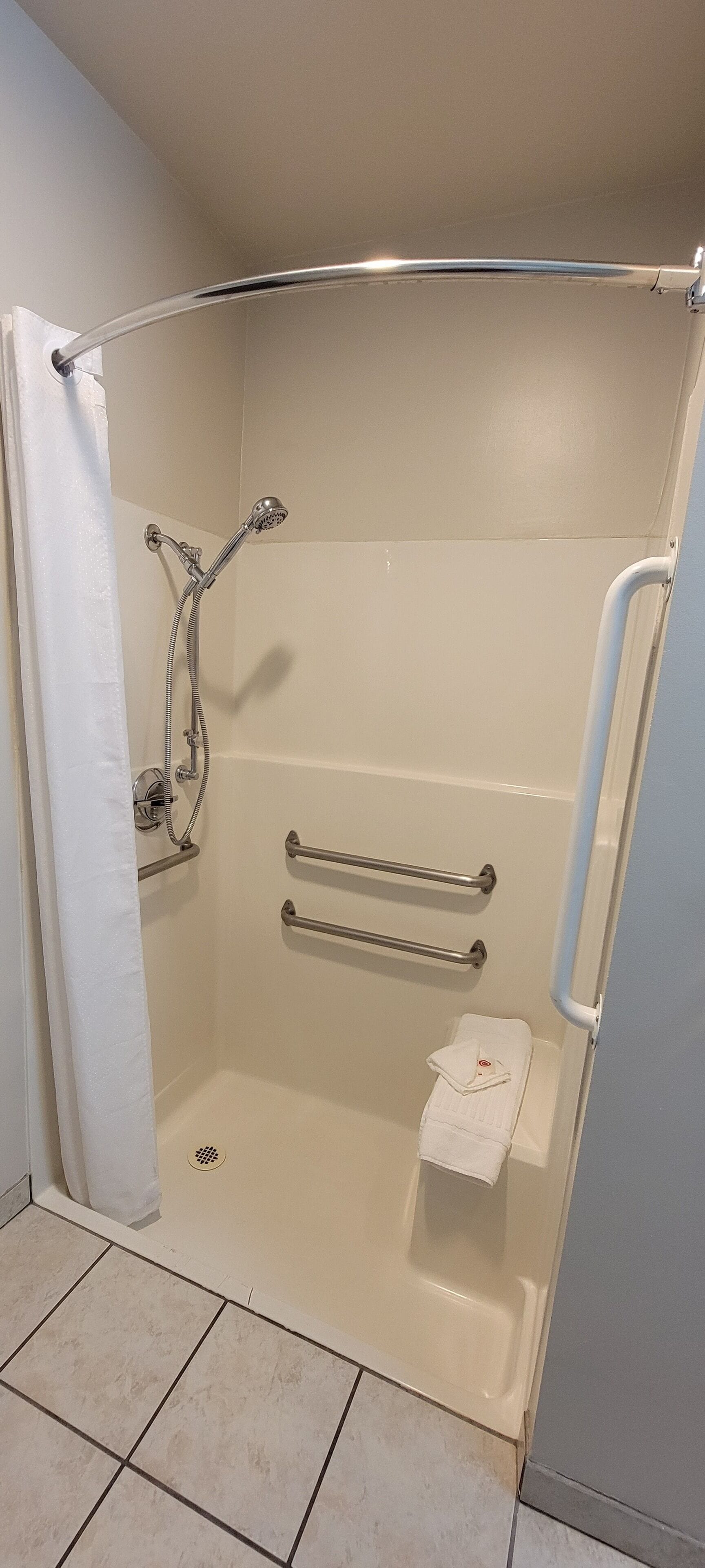 Eine barrierefreie Dusche mit Haltegriff, einem weißen Handtuch und einer Duschbrause.