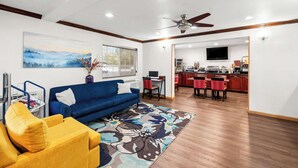 A living room with a blue sofa, yellow armchair, and a colorful rug. There is a dining area with red chairs and a kitchen in the background. - Comfort Inn Yreka I-5 (Yreka)