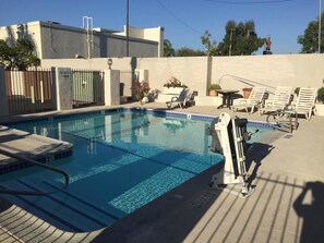 A swimming pool with a lifeguard chair, lounge chairs, and a pool ladder. - Queens Inn Anaheim (Anaheim)