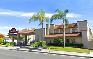 A hotel with a sign reading "Queens Inn Anaheim," featuring a two-story building with a red-tiled roof, palm trees, and a well-maintained lawn. - Queens Inn Anaheim (Anaheim)