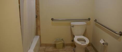Un baño pequeño para una sola persona, con inodoro, barra de apoyo, cortina de ducha y cubo de basura.