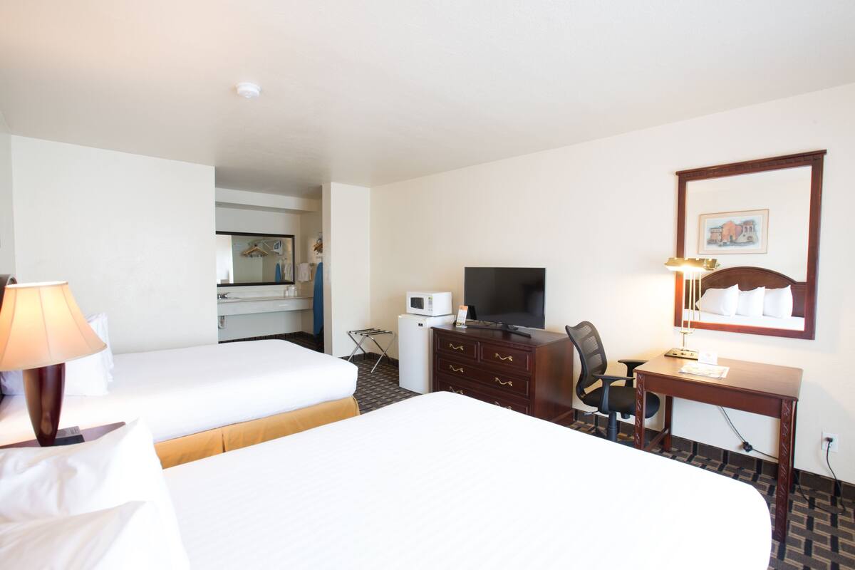 A hotel room with two beds, a desk, a chair, a television, a microwave, and a small refrigerator.