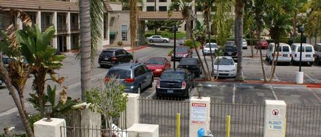 A hotel with a swimming pool, palm trees, and a parking lot with cars.
