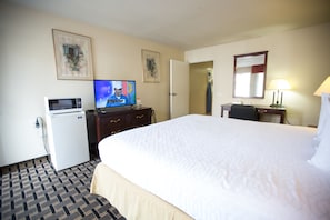 A hotel room with a large bed, a television, a desk with a lamp, and a refrigerator. - Queens Inn Anaheim (Anaheim)