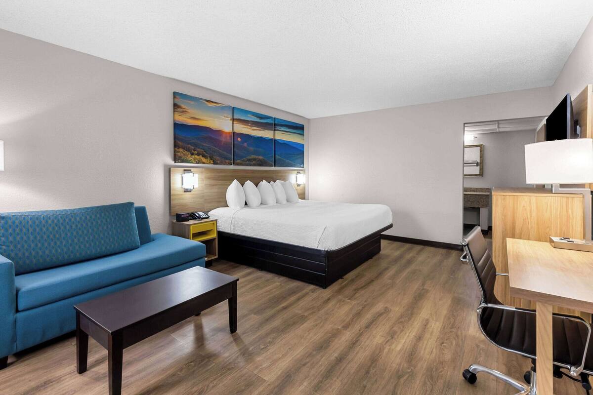 A hotel room with a bed, a sofa, a desk, and a painting on the wall.
