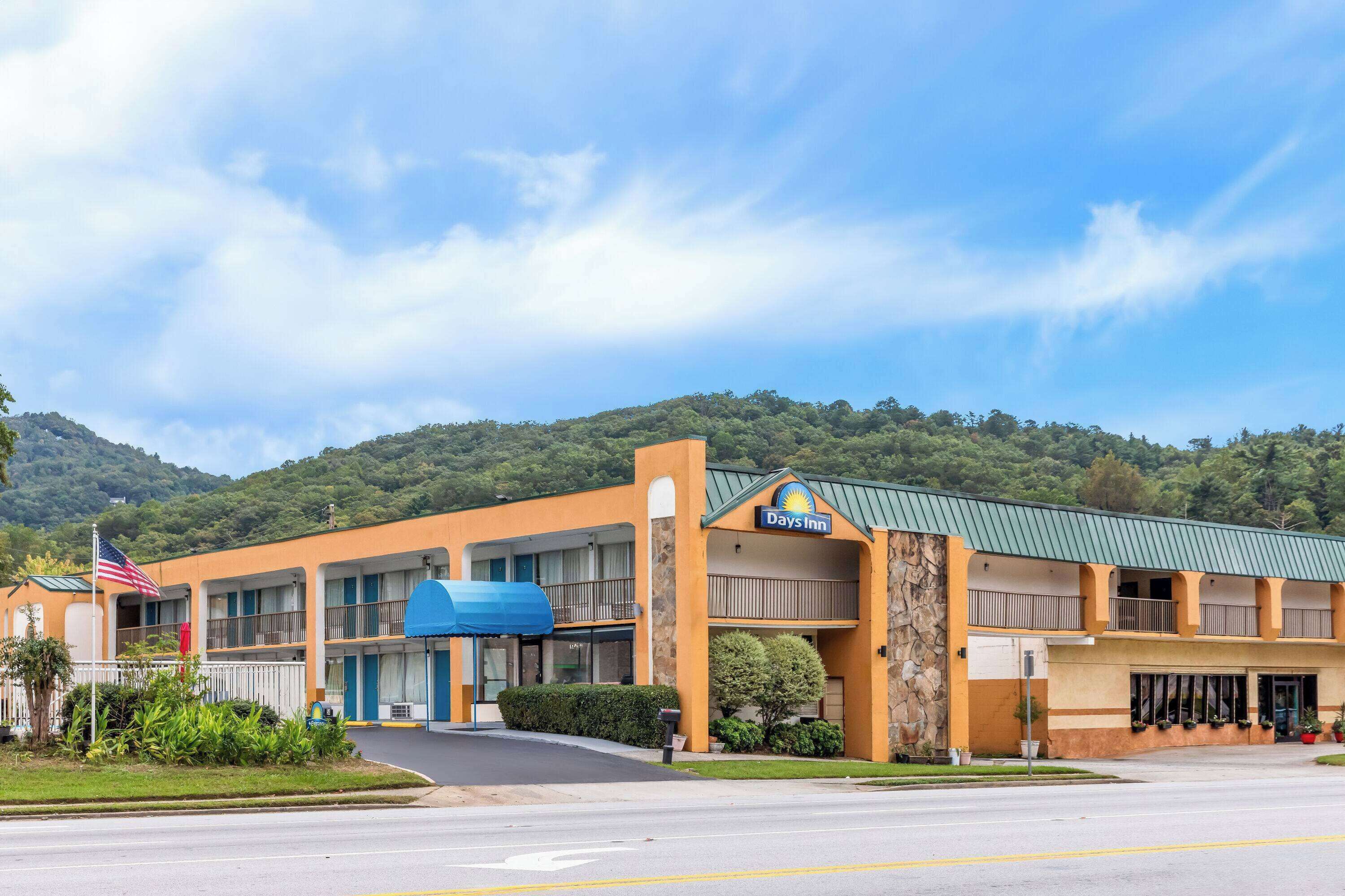 A Days Inn with a two-story structure, a covered parking area, and a view of a hilly landscape.