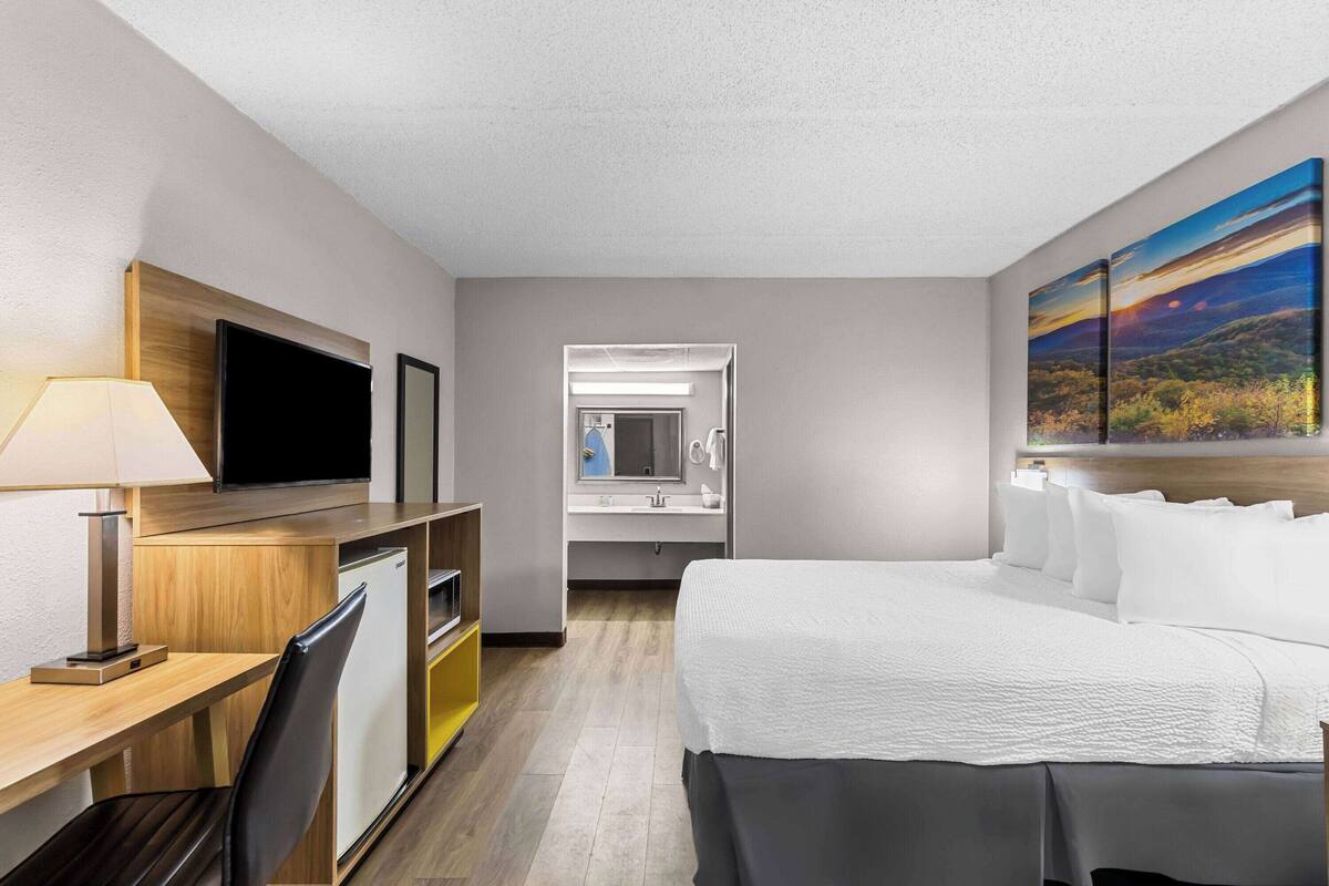 A hotel room with a bed, desk, TV, and a bathroom visible through an open door.