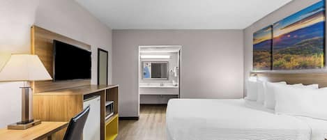 Habitación de hotel con cama, escritorio, televisor y baño visible a través de una puerta abierta.