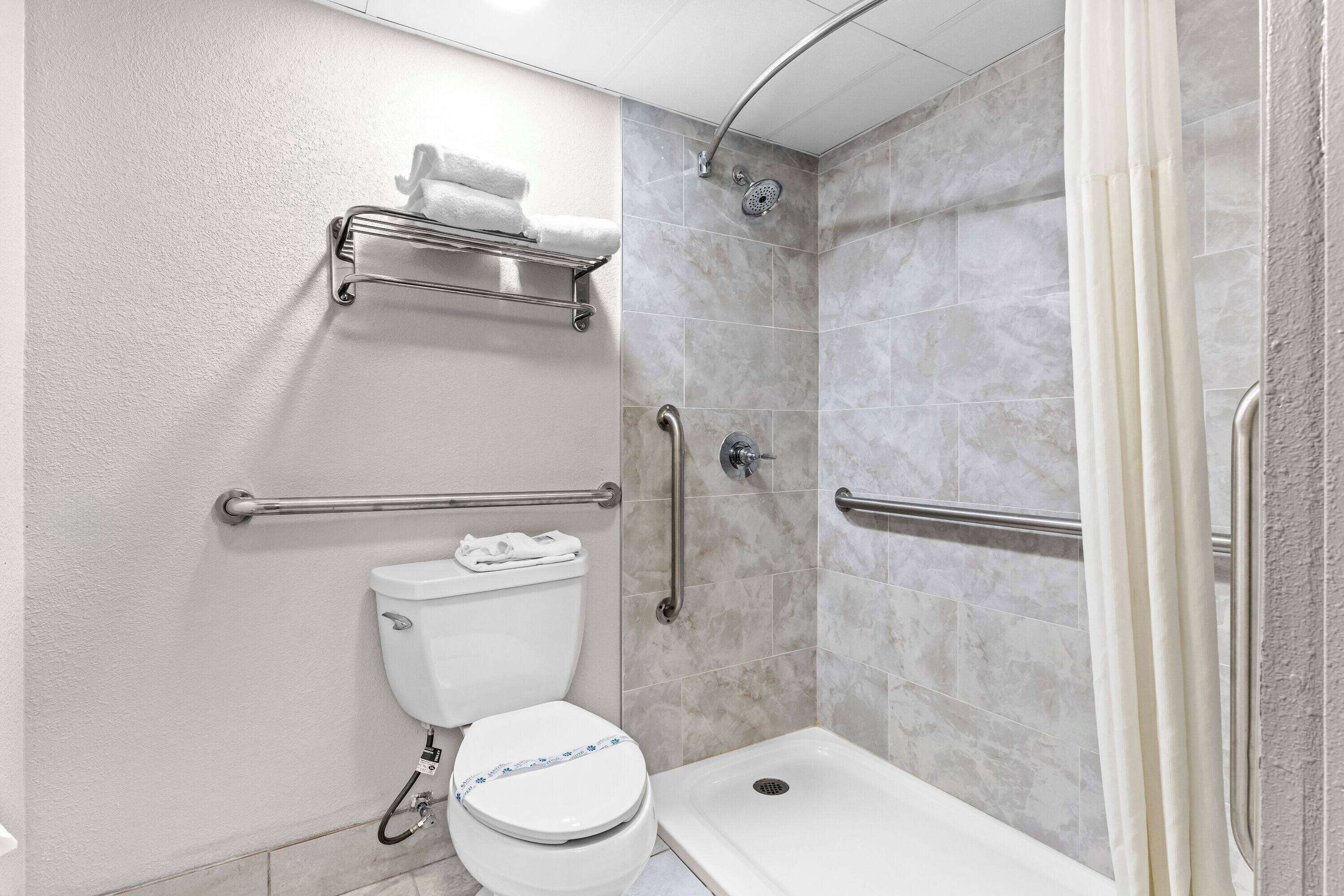 Un baño con inodoro, ducha y barras de apoyo.