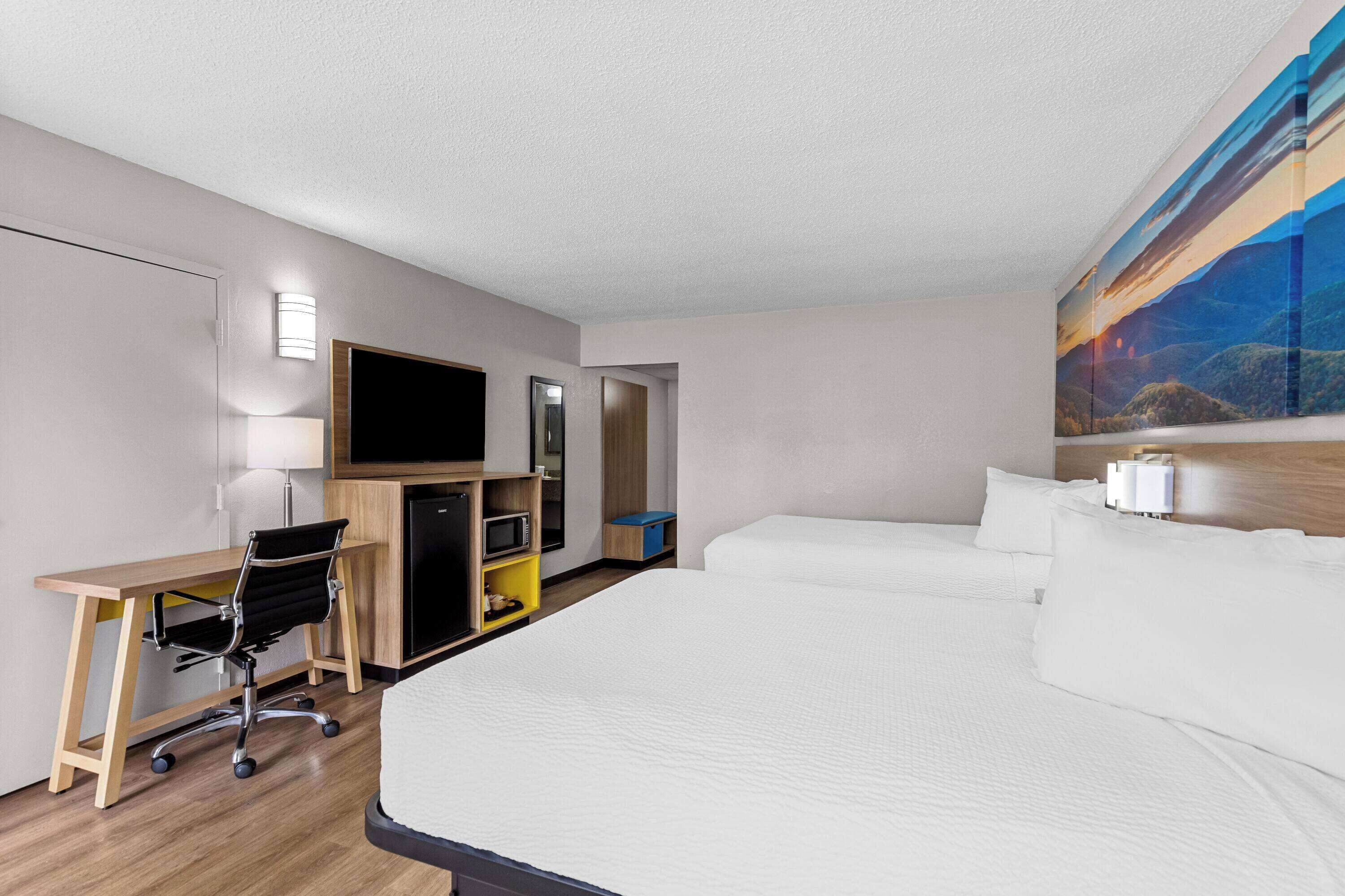 A hotel room with a large bed, a desk with a chair, a television, and a painting on the wall.
