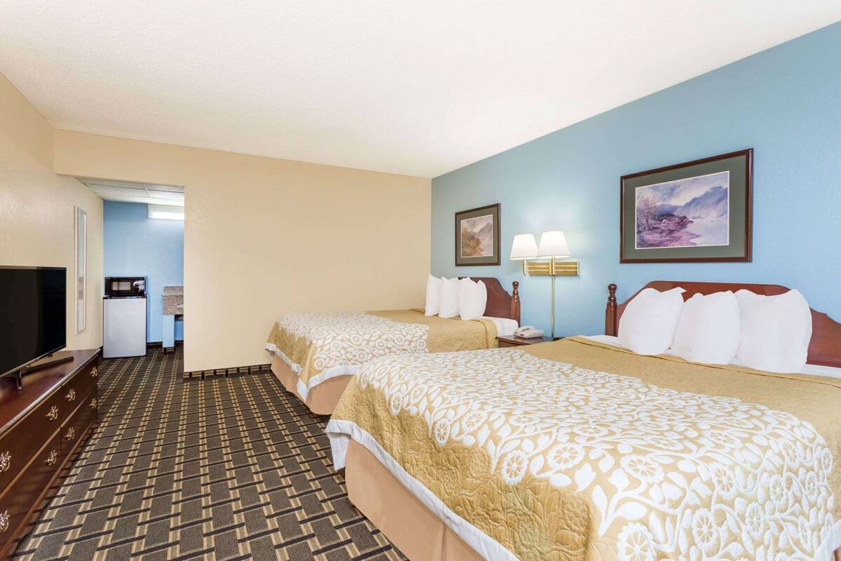 A hotel room with two beds, a television, a refrigerator, and a microwave.