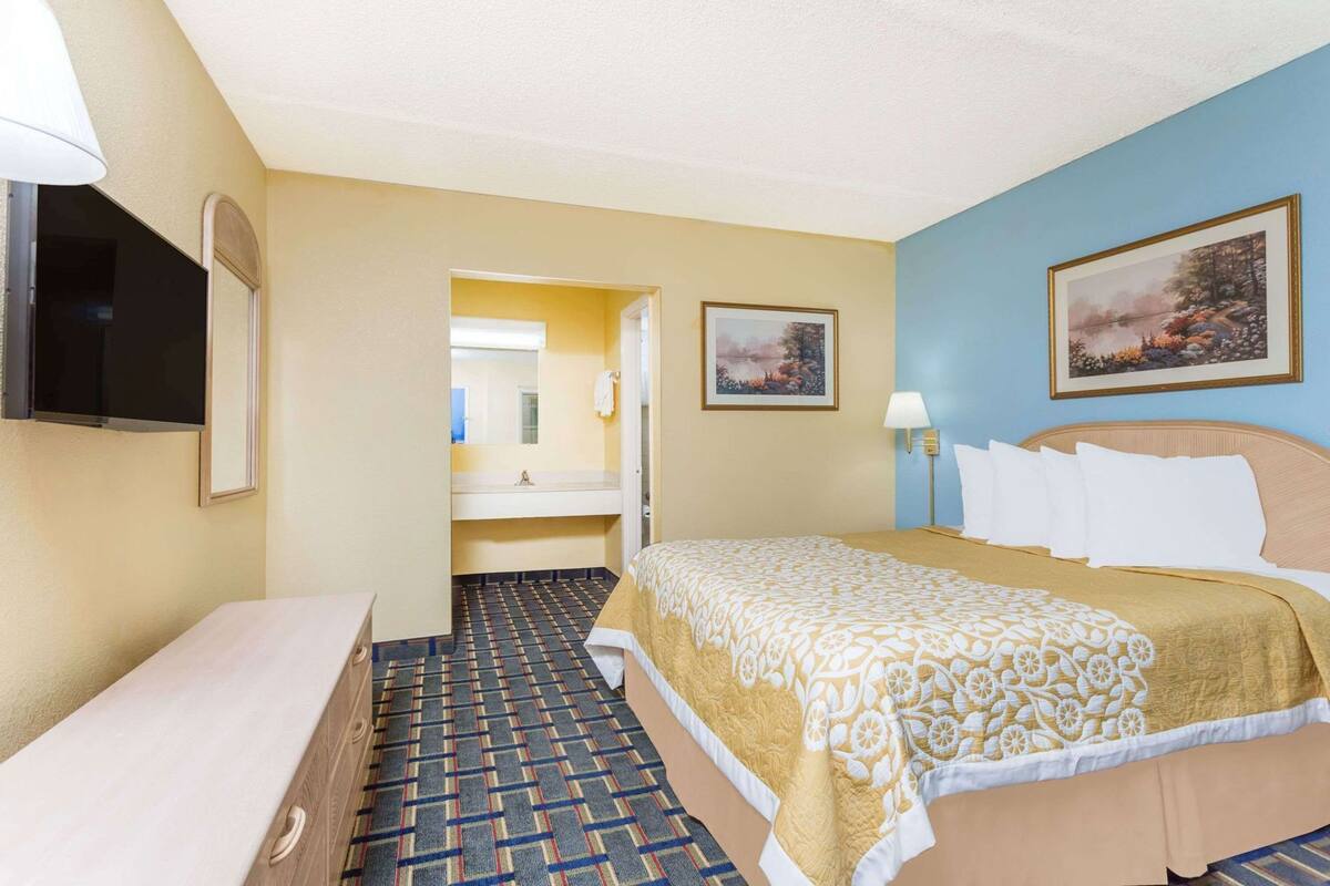 A hotel room with a bed, a TV, a bathroom, and a painting on the wall.