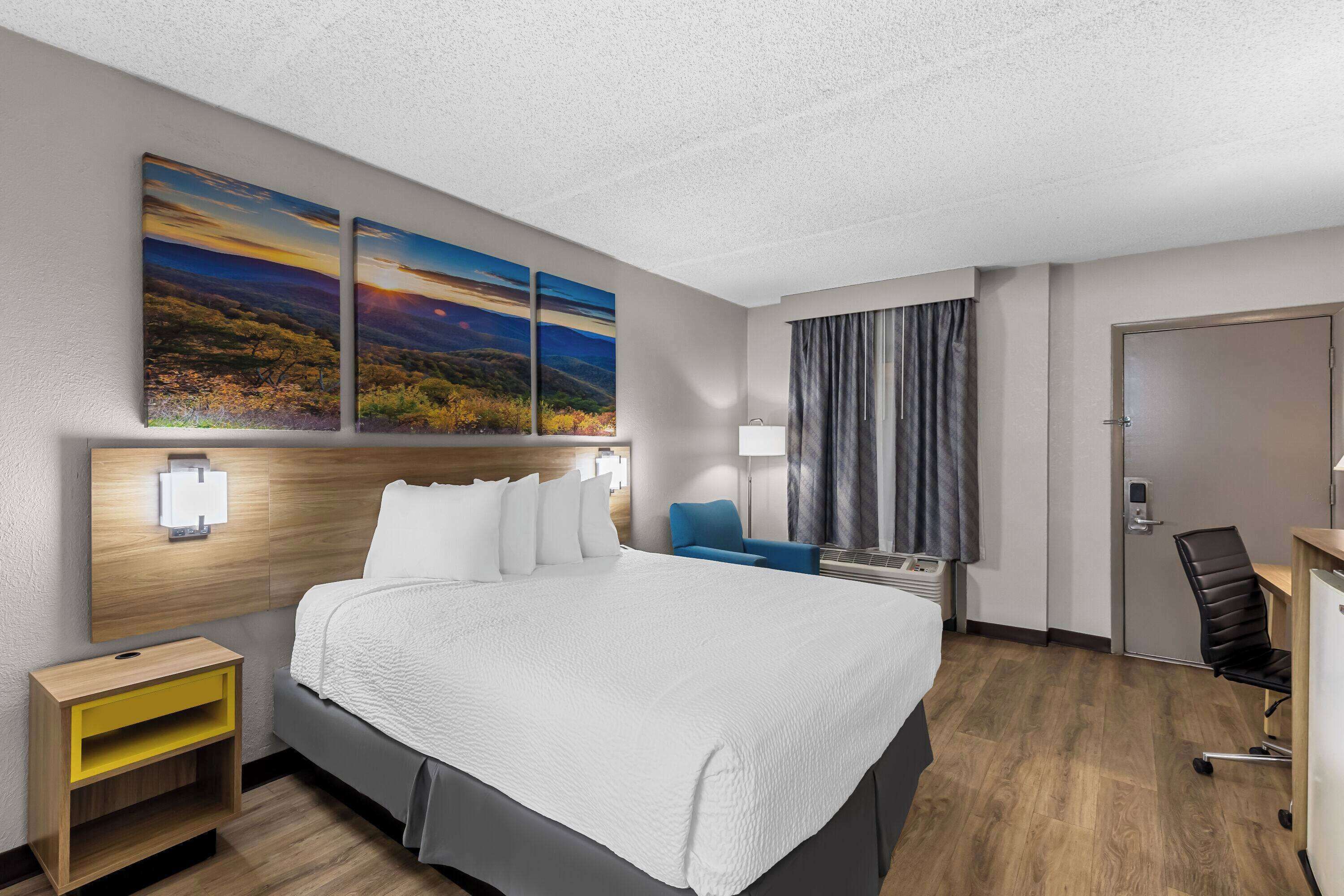 A hotel room with a large bed, a desk, a chair, a nightstand, and two wall-mounted lamps.