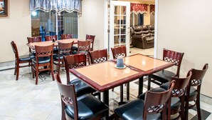 A dining area with a wooden table and chairs, a glass partition, and a leather couch in the background.