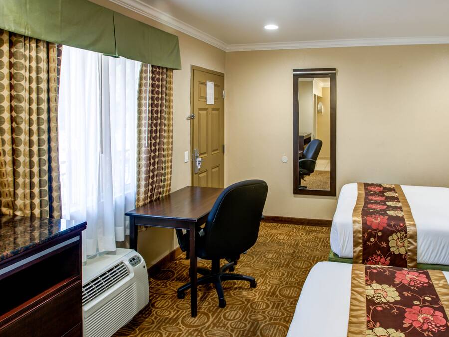 Habitación de hotel con dos camas, un escritorio, una silla, un espejo y una ventana con cortinas.