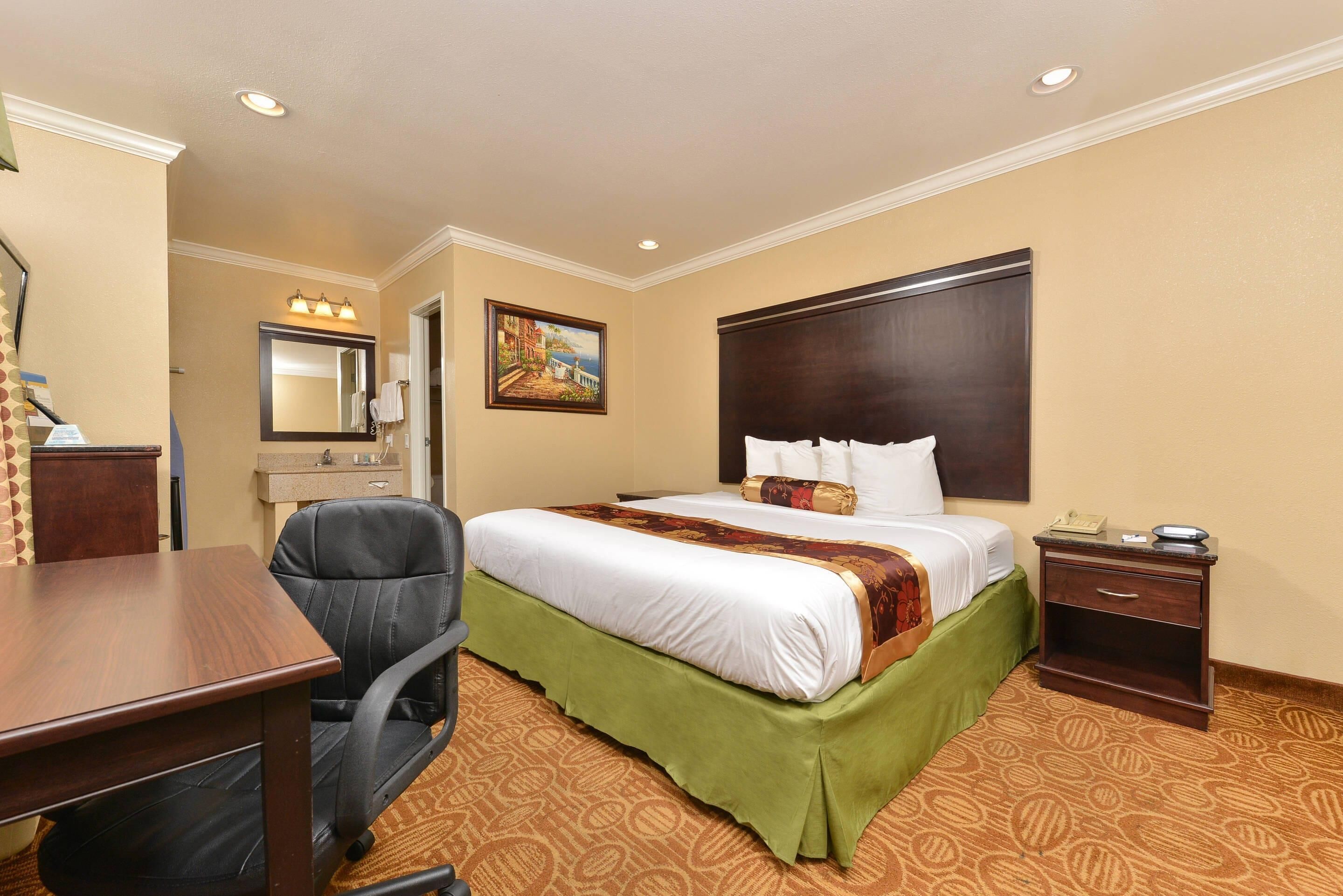Une chambre d’hôtel avec un lit, un bureau, une chaise et un tableau au mur.