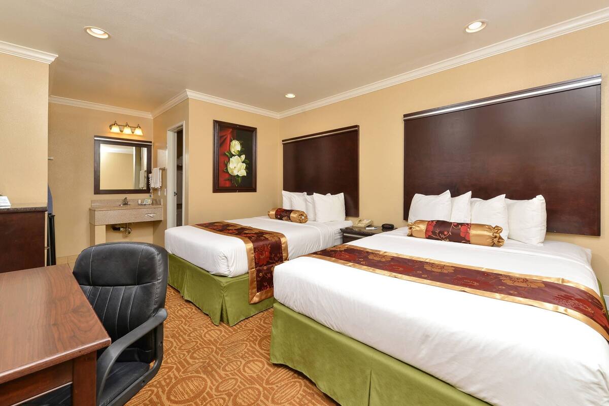 A hotel room with two beds, a desk, a chair, a mirror, and a painting.